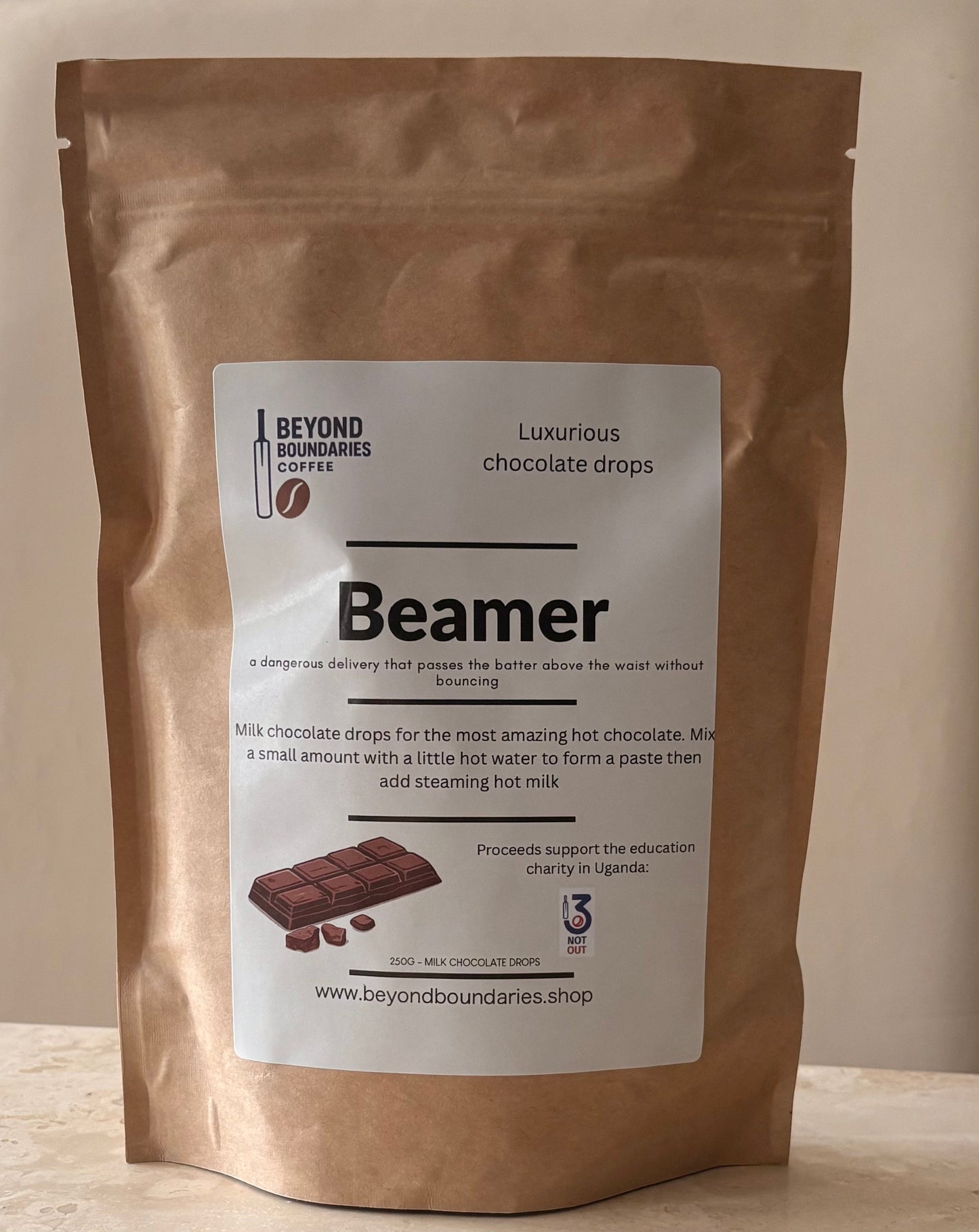 A stand-up kraft paper pouch of Beyond Boundaries Chocolate 'Beamer' chocolate drops, featuring a white label with product details and a chocolate bar illustration, set against a neutral beige background.