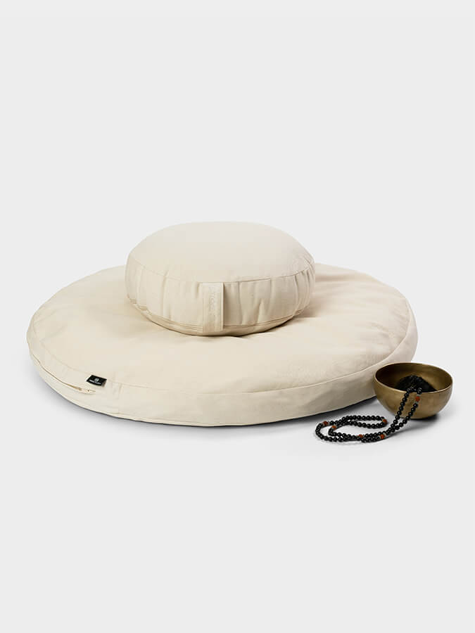 Beige meditation pillow with a small bowl and necklace on a white background