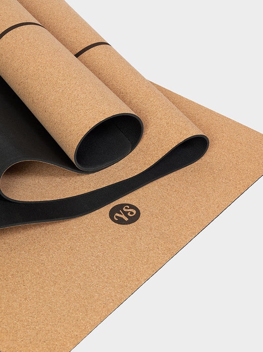 Cork yoga mat with black strap on a light gray background