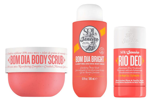 Three Sol Janeiro body care products on a white background: a round pink scrub container labeled 'BOM DIA BODY SCRUB,' a tall coral body wash bottle labeled 'BOM DIA BRIGHT,' and a matching coral deodorant stick labeled 'RIO DEO.'.